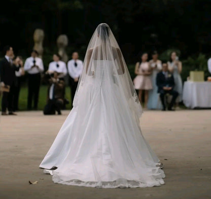 Bride in a white wedding dress with a long veil walking down the aisle outdoors with guests in the background.