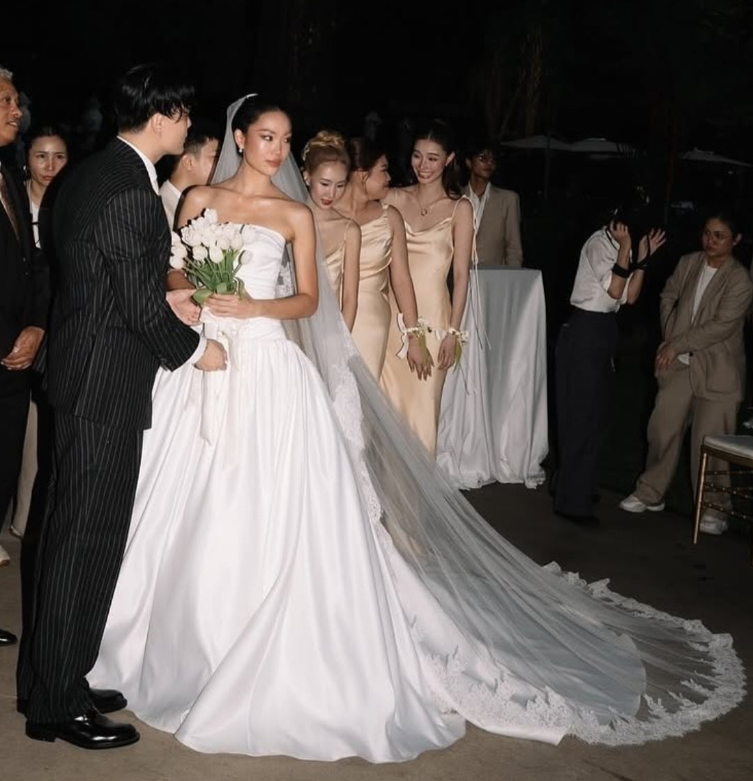 Wedding scene with a bride in a white gown and a groom in a black suit, surrounded by bridesmaids in beige dresses.
